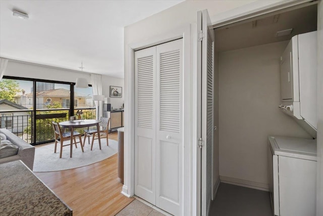 washroom with estacked washer and dryer, light wood finished floors, and baseboards