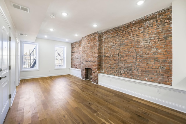 unfurnished living room featuring a brick fireplace, brick wall, and wood-type flooring