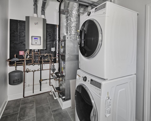 washroom with water heater, stacked washing maching and dryer, and dark tile patterned flooring