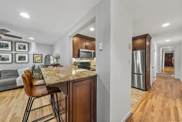 607 1st St Unit 1, Hoboken, NJ 07030 - kitchen featuring appliances with stainless steel finishes, a baseboard radiator, light stone counters, light wood-type flooring, and a kitchen bar