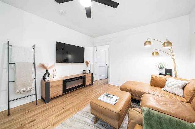 living area with a glass covered fireplace, baseboards, light wood-type flooring, and a ceiling fan