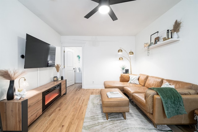 living area featuring a glass covered fireplace, baseboards, light wood-style flooring, and a ceiling fan