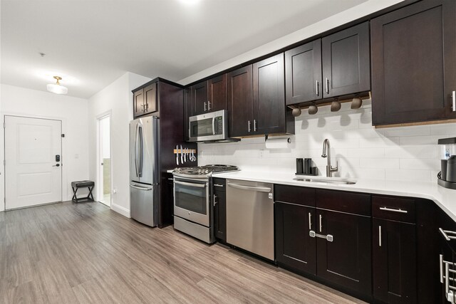 kitchen featuring appliances with stainless steel finishes, sink, decorative backsplash, dark brown cabinetry, and light hardwood / wood-style floors