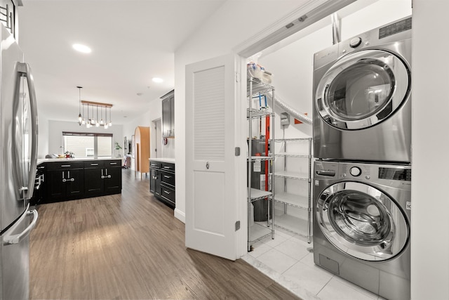 laundry area featuring stacked washer and dryer, an inviting chandelier, and light hardwood / wood-style flooring