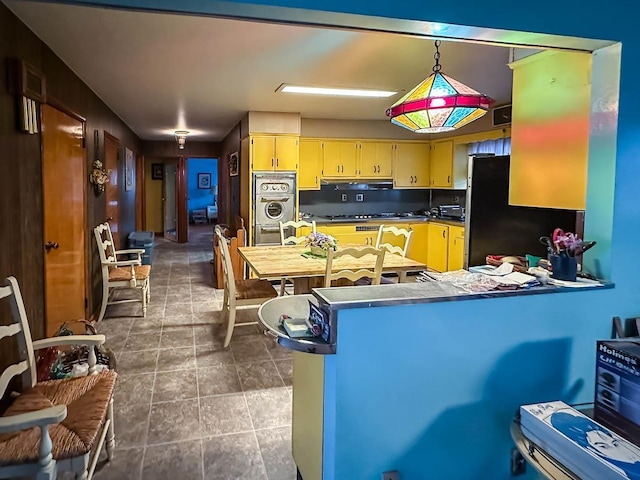 kitchen with under cabinet range hood, a peninsula, cream cabinets, freestanding refrigerator, and washer / clothes dryer