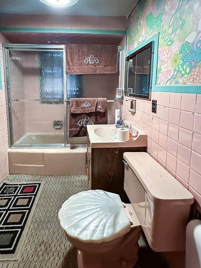 bathroom featuring toilet, tile walls, vanity, and shower / bath combination with glass door