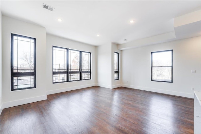 unfurnished room with visible vents, plenty of natural light, baseboards, and dark wood finished floors