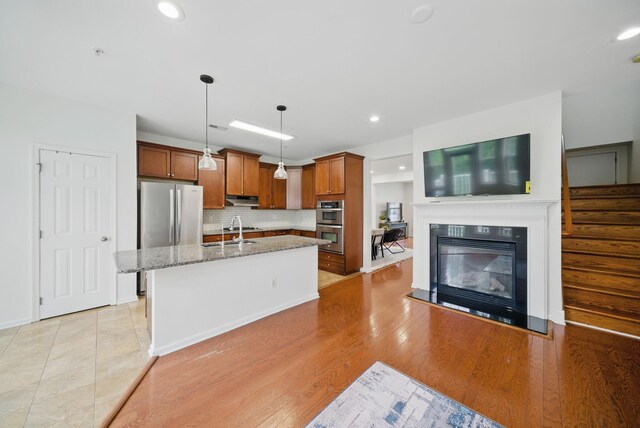 28 Creekside Ct Unit 28, Secaucus, NJ 07094 - kitchen with stainless steel appliances, brown cabinets, light stone countertops, tasteful backsplash, and a center island with sink
