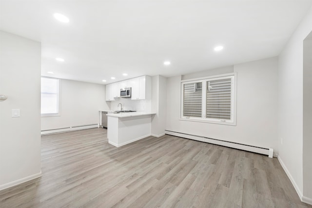 interior space with baseboard heating, kitchen peninsula, stainless steel appliances, and white cabinetry