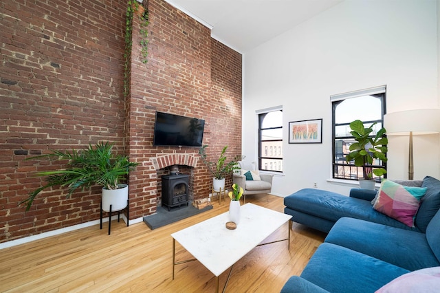 living area with high vaulted ceiling, wood finished floors, brick wall, baseboards, and a wood stove