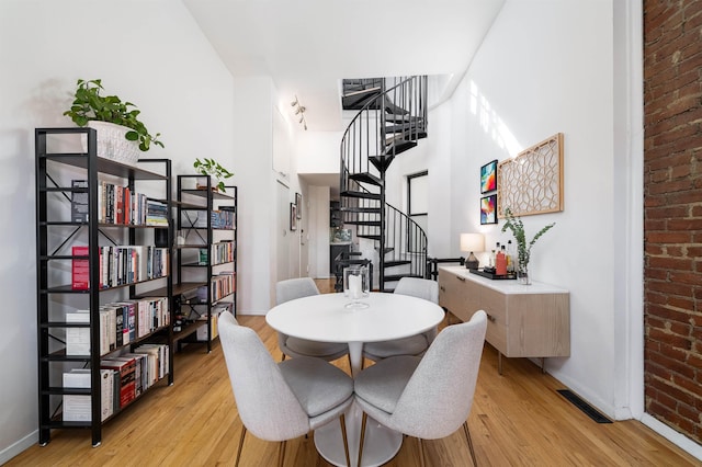 dining space featuring stairway, light wood-style flooring, baseboards, and brick wall