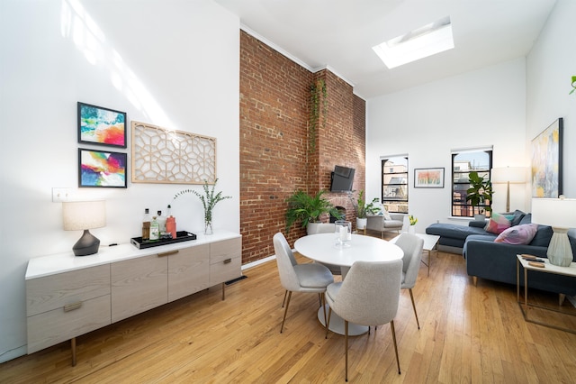 dining area featuring visible vents, high vaulted ceiling, light wood-style flooring, a skylight, and brick wall