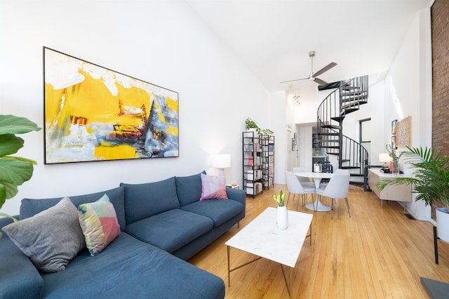 living area featuring stairs, wood finished floors, a towering ceiling, and a ceiling fan