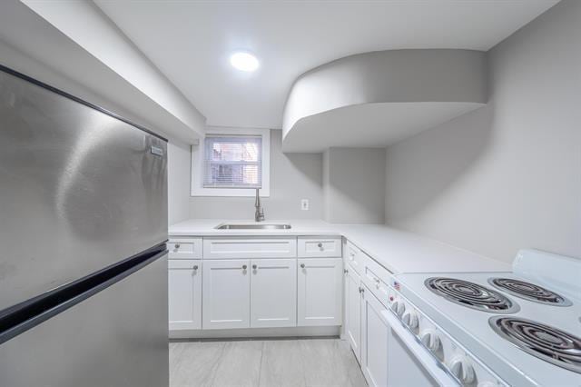 kitchen with sink, white electric range oven, white cabinetry, and stainless steel refrigerator