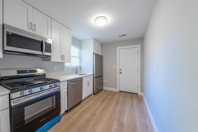 kitchen featuring stainless steel appliances, white cabinetry, sink, and light hardwood / wood-style floors