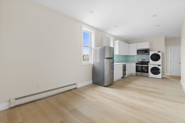 kitchen with stainless steel appliances, a baseboard radiator, stacked washing machine and dryer, tasteful backsplash, and light wood finished floors
