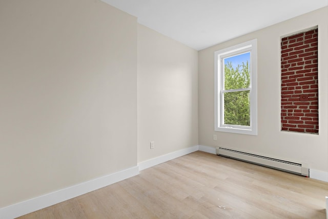 spare room with baseboard heating, light wood-style flooring, and baseboards