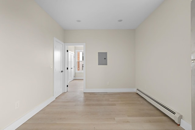 spare room with a baseboard heating unit, light wood-type flooring, baseboards, and electric panel