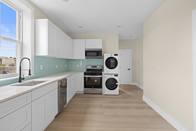 kitchen with appliances with stainless steel finishes, a sink, stacked washer and clothes dryer, baseboards, and backsplash