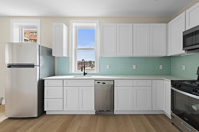 kitchen with stainless steel appliances, a sink, light wood finished floors, and light countertops