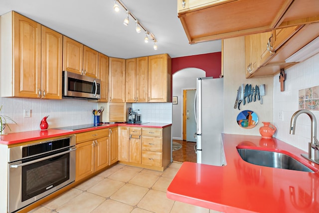 kitchen with a sink, decorative backsplash, arched walkways, and appliances with stainless steel finishes