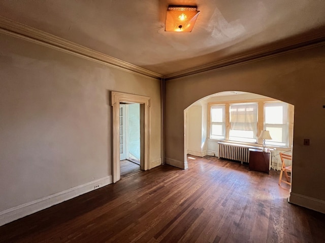 empty room featuring dark wood-type flooring, radiator heating unit, and crown molding