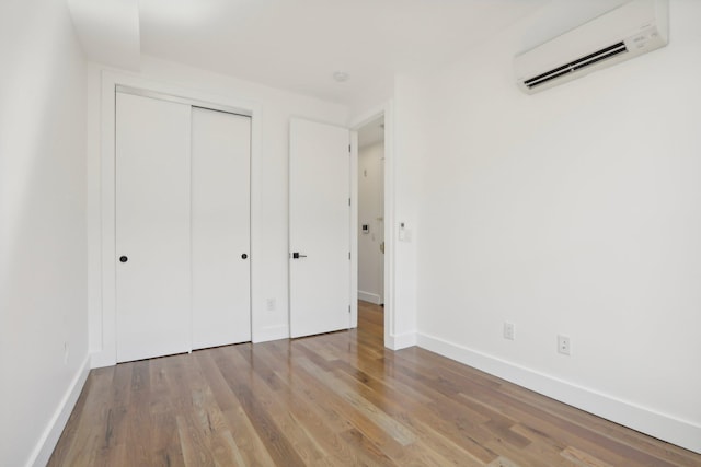 unfurnished bedroom with a closet, baseboards, an AC wall unit, and wood finished floors