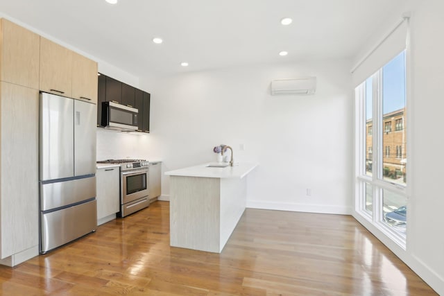 kitchen with sink, light hardwood / wood-style flooring, an AC wall unit, kitchen peninsula, and stainless steel appliances