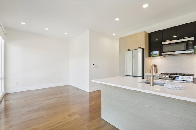 kitchen featuring light countertops, appliances with stainless steel finishes, light wood finished floors, modern cabinets, and tasteful backsplash