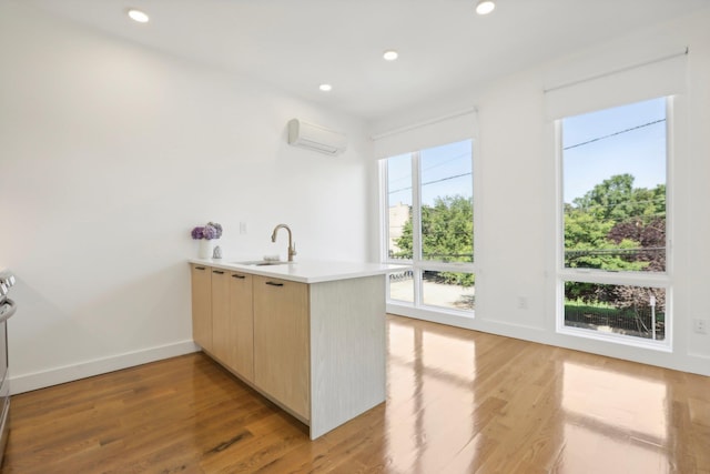 kitchen with light brown cabinetry, sink, an AC wall unit, kitchen peninsula, and light hardwood / wood-style floors