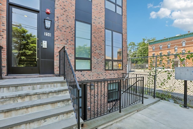 view of exterior entry featuring brick siding and fence