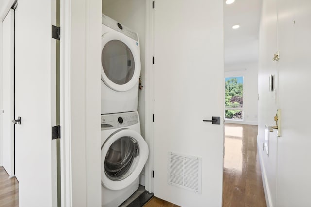 clothes washing area with stacked washer and clothes dryer and wood-type flooring