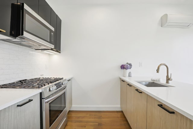 kitchen featuring stainless steel appliances, light countertops, light wood-style flooring, decorative backsplash, and a sink