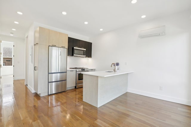 kitchen with stainless steel appliances, light wood finished floors, a wall mounted AC, and a peninsula