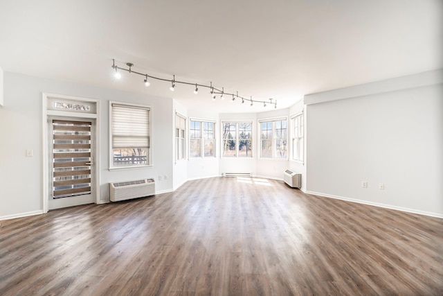 unfurnished living room with a wall unit AC, wood finished floors, baseboards, track lighting, and a baseboard heating unit