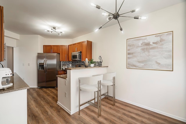 kitchen featuring backsplash, dark wood finished floors, appliances with stainless steel finishes, a peninsula, and brown cabinetry