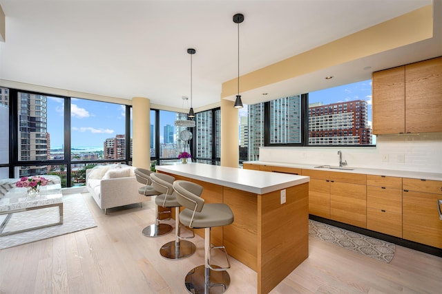 kitchen with tasteful backsplash, floor to ceiling windows, a kitchen island, sink, and light wood-type flooring