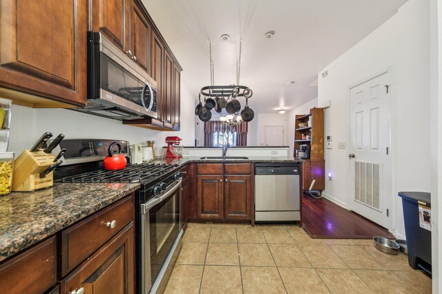 265 Custer Ave Unit 103, Jersey City, NJ 07305 - kitchen featuring appliances with stainless steel finishes, a peninsula, a chandelier, dark stone counters, and light tile patterned floors