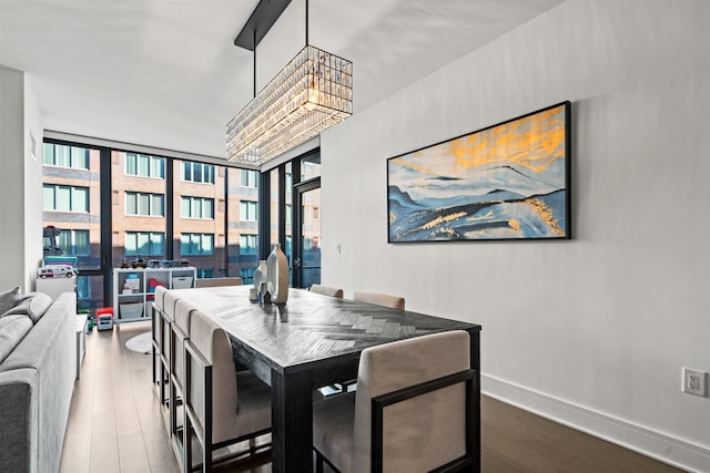 dining area featuring a wall of windows, a chandelier, baseboards, and wood finished floors