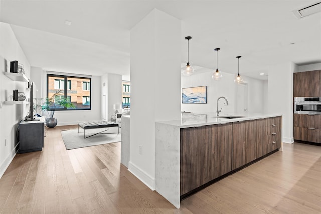 kitchen featuring light wood finished floors, modern cabinets, light countertops, stainless steel oven, and a sink