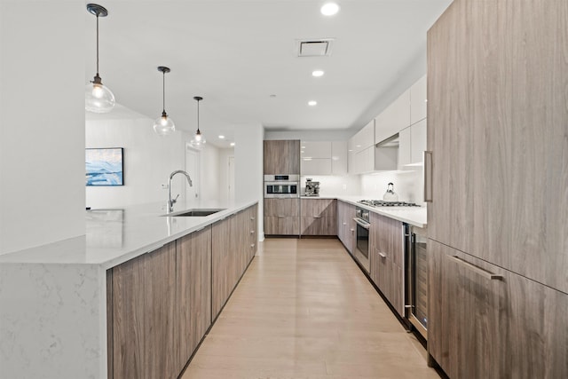 kitchen featuring a sink, stainless steel oven, white cabinetry, modern cabinets, and decorative light fixtures