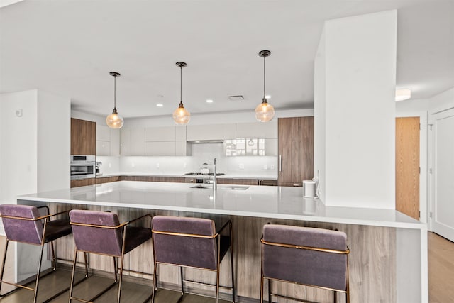 kitchen with pendant lighting, light countertops, white cabinets, modern cabinets, and a kitchen bar