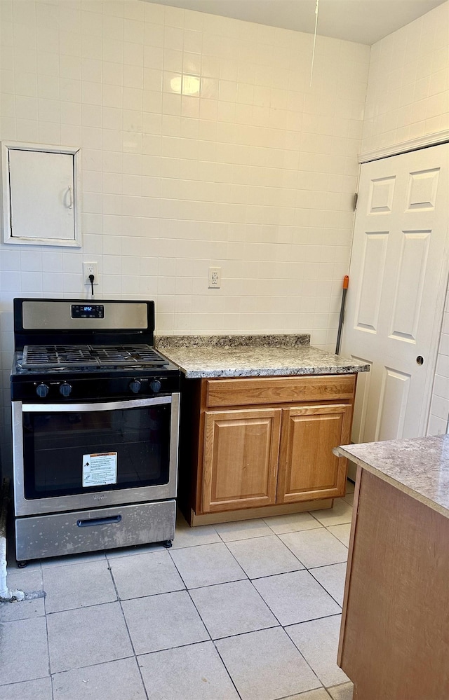 kitchen with tasteful backsplash, brown cabinetry, light tile patterned flooring, gas stove, and tile walls