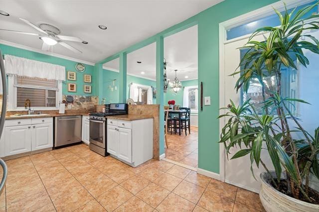 kitchen featuring ceiling fan with notable chandelier, stainless steel appliances, sink, light tile patterned floors, and white cabinets