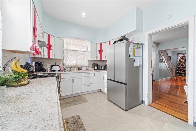 kitchen with backsplash, stainless steel fridge, and white cabinets