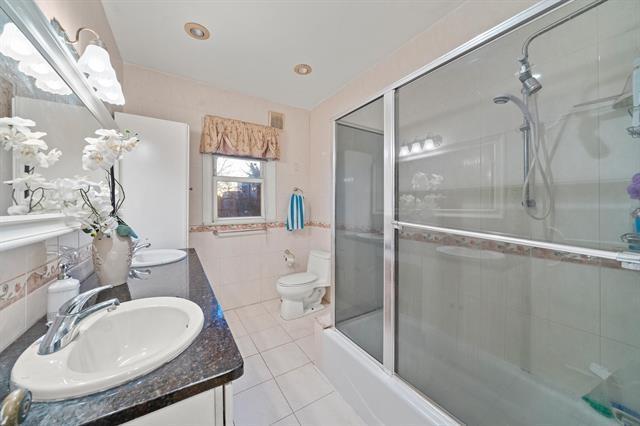 full bathroom featuring bath / shower combo with glass door, vanity, tile walls, tile patterned flooring, and toilet