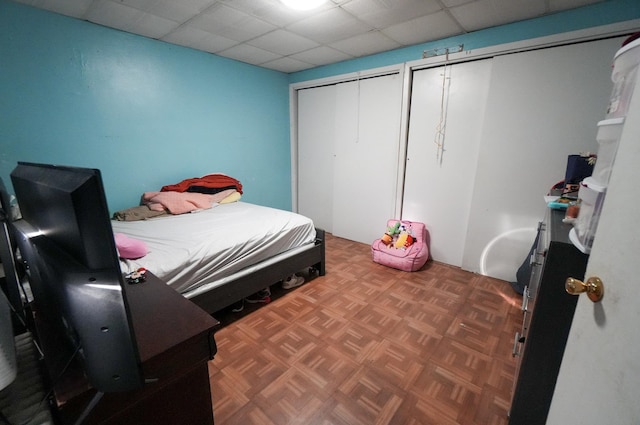 bedroom featuring parquet flooring, two closets, and a drop ceiling