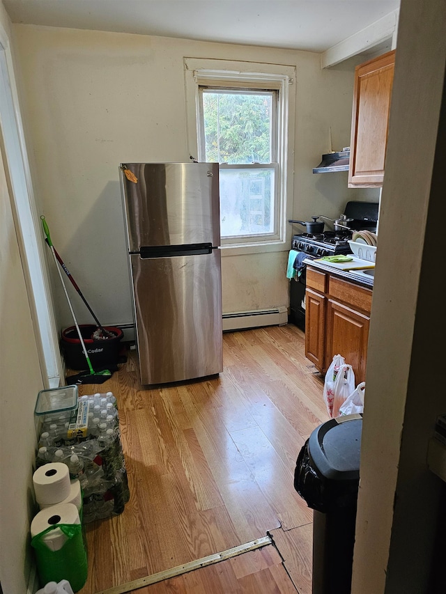 kitchen with stainless steel fridge, gas stove, a baseboard heating unit, light hardwood / wood-style floors, and range hood