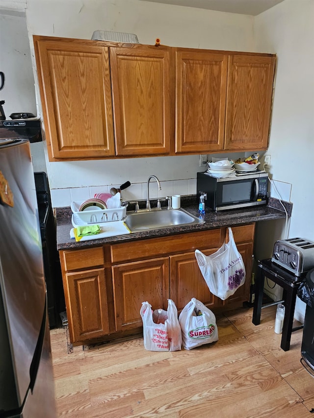 kitchen featuring dark stone countertops, sink, light hardwood / wood-style flooring, and appliances with stainless steel finishes