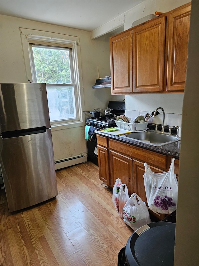 kitchen featuring sink, range hood, a baseboard heating unit, stainless steel fridge, and light hardwood / wood-style floors